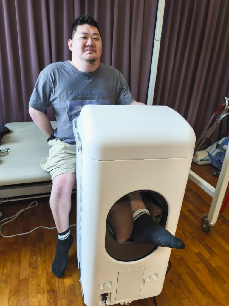 Ben, MDAS member, is seated on a bed with left leg positioned in the BIXEPS.